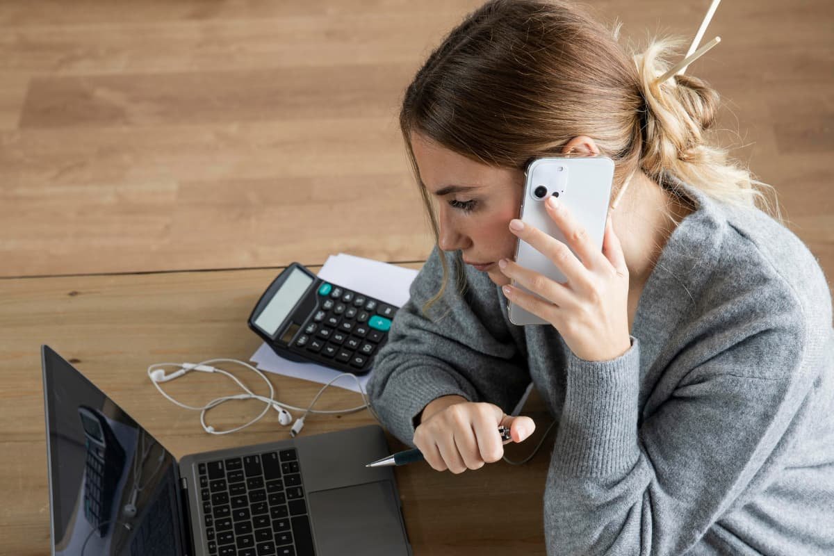 Pessoa analisando uma conta telefônica no laptop para encontrar maneiras de reduzir custos em telefonia, com uma calculadora ao lado.