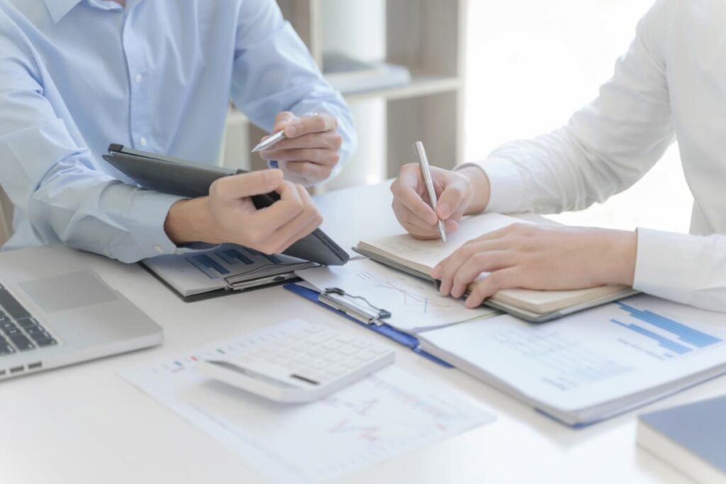 Dois profissionais discutindo sobre CAPEX e OPEX, analisando gráficos financeiros e fazendo anotações em um escritório.