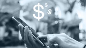 Pessoa utilizando um celular com um cifrão em cima dele.