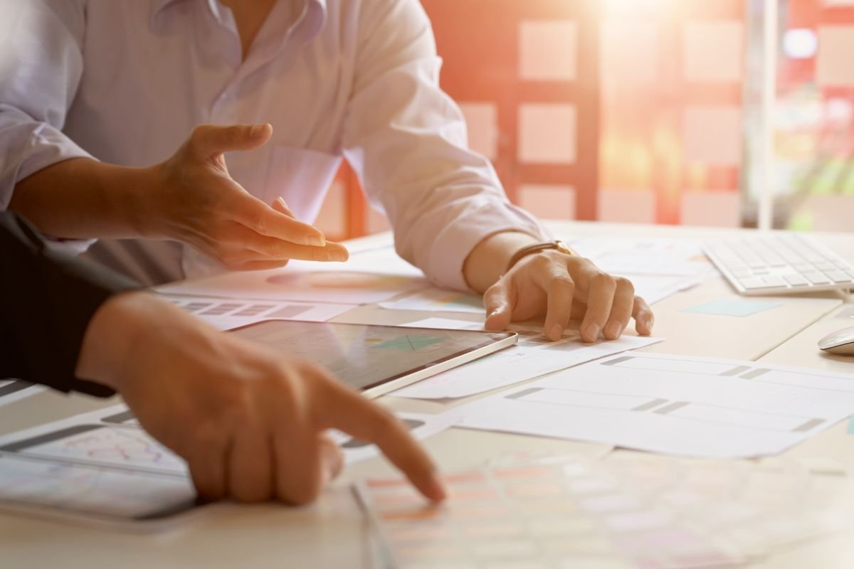 Duas pessoas discutindo uma estratégia, apontando para papéis e documentos sobre uma mesa.