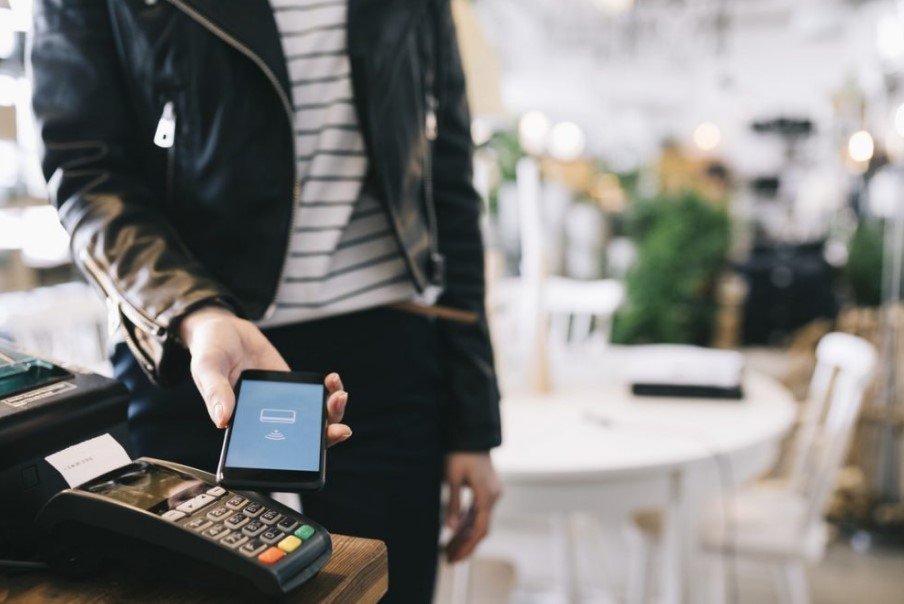 Mulher realizando pagamento com o celular, aproximando-o da máquina