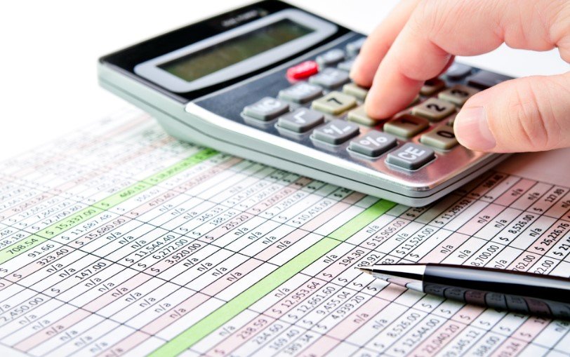 Pessoa utilizando uma calculadora ao lado de uma caneta sobre uma planilha com gastos.