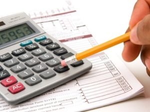 Pessoa com um lápis na mão, usando ele para pressionar botão de igual em uma calculadora.